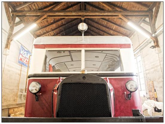 Die in ihrer Form an einen alten LKW erinnernde Schnauze eines historischen Schienenbusses aus den 1930er-Jahren in Weitwinkelperspektive; das Fahrzeug steht in einem Lokschuppen, dessen hölzerne Dachkonstruktion über dem Schienenbus zu sehen ist.