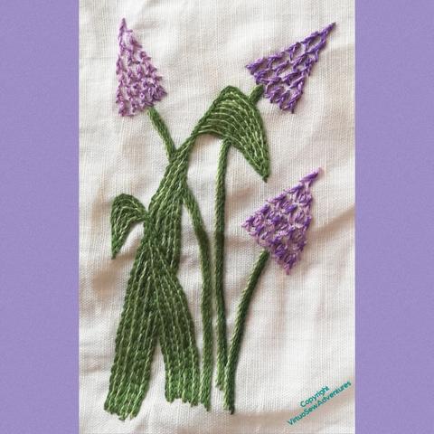 Hand embroidery of grape hyacinths, bordered with lilac panels. The leaves are stem stitch filling and the florets are stacked for stitches.