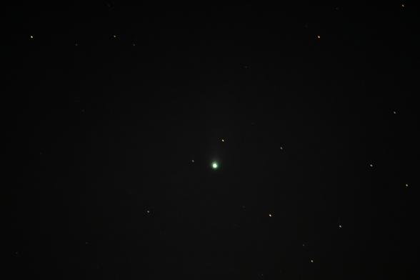 A low-quality photo of a night sky with some stars and a green comet near the center.