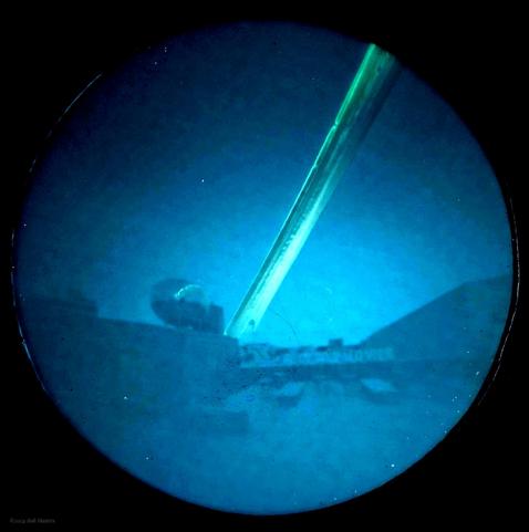 A blue circle in a black background. The blue circle has a yellow-green stripe from top right to near the centre of the lower third. There is a circular object near the base of the stripe, and a sign below it.