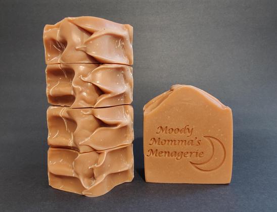 On the left are 4 bars of bronze soap stacked on their side to show the top detail. The bar on the right in stamped with "Moody Momma's Menagerie" and a crescent moon