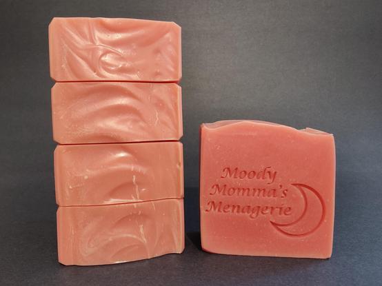 On the left are 4 bars of pink soap stacked on their side to show the top detail. The bar on the right in stamped with "Moody Momma's Menagerie" and a crescent moon
