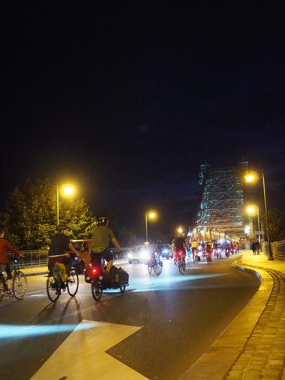 Eine CM aus Radfahrer*innen vor dem Blauen Wunder. Es ist abends und dunkel, Straße & Räder sind erleuchtet