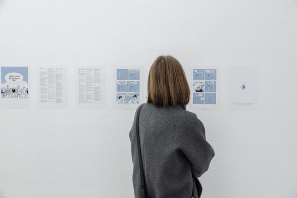A female-presenting exhibtion visitor from behind, reading the last pages of the comic. They even printed out the annotations!