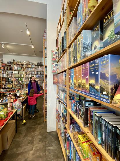 Ein Gang im Brettspielgeschäft mit hohen Regalen voll mit Brettspielen und normalen Tischen mit Kartenspielen