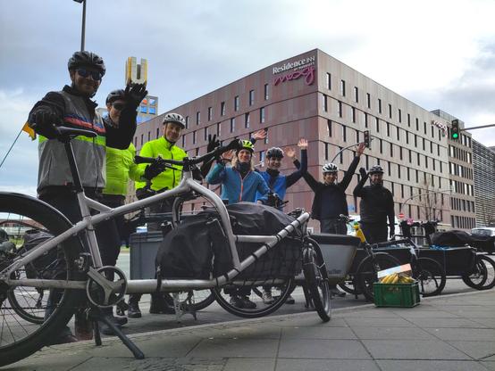Vor dem Dortmunder U stehen einige verschiedene Lastenräder. Sechs Personen in Fahrradkleidung winken in die Kamera