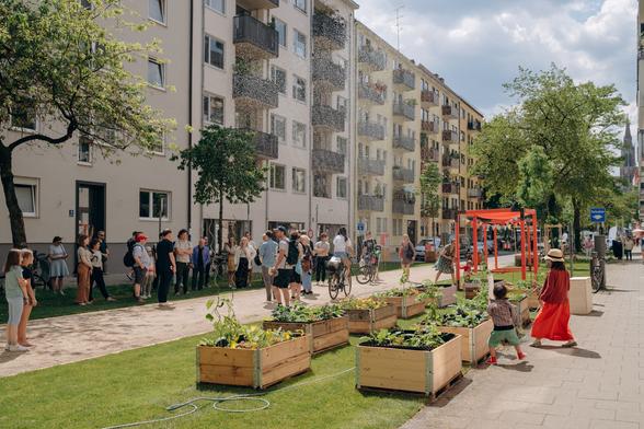 MCube subproject in the Kolumbusstraße in the Munich Au, which was temporarily greened and closed to vehicles in 2023: "Car-reduced quarters for a more livable city (AQT)". Citizens standing and walking in the street at the kick-off event.