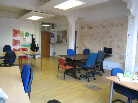 Photo of an office with a few tables surrounded by chairs.  One wall is covered with a large - about 2m by 3m - doodlebot artwork