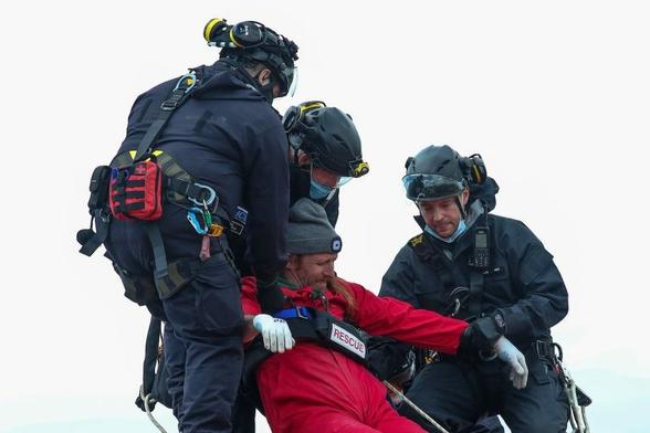 A photograph of a climbing team securing a protestor in red overalls to remove them from the roof.