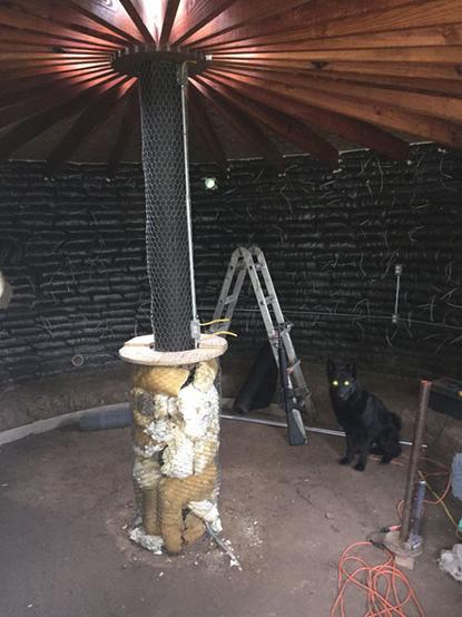 round earthbag structure with a telephone pole in the center that supports a radial network of rafters leading to the walls.