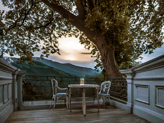 Wrought iron chairs and table with a magical light, on a balcony overlooking mountains and a sunset.