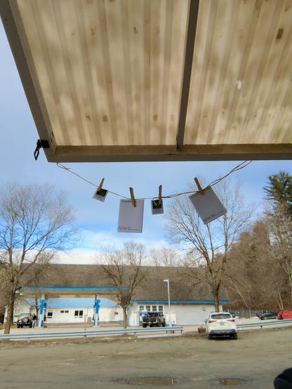 Two zines hang from a clothesline on an overhang at KS Coffee; 8 VT Route 17