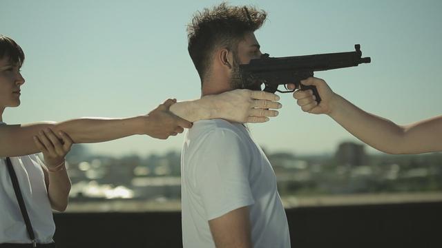 В кадре три перформер:ки на крыше в солнечную погоду исполняют медленные хореографические движения. Одна перформерка положила муляж человеческой руки на плечо к перформеру, который стоит к ней спиной. Другая перформерка приставила с другой стороны к искусственной руке имитацию огнестрельного оружия с двумя рукоятками. Дуло ружья направлено на ту, кто это оружие держит. Перформанс исполняется в белых ти-шортках и со сосредоточенными лицами. // In the still, three performers on the roof in sunny weather perform slow choreographic movements. First female performer placed a dummy of a human hand on the shoulder of the second male performer, who stood with his back to her. Third female performer placed an imitation firearm with two handles on the other side of the artificial hand. The muzzle of the gun is pointed at the third person. The performance is performed in white T-shorts and with concentrated faces. // Elena Artemenko, “Soft Power”, 2016, video