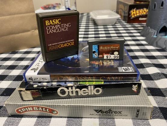 A collection of old games -- BASIC for the Atari 400/800, Broken Sword The Shadow of the Templars for GBA (price: $7.00), Colossal Cave in a PS5 game case, Othello in a NES game case, Spinball in a Vectrex game case.