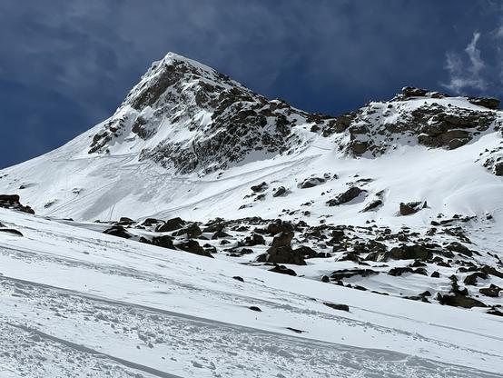 The sharp summit of a rocky, snow-covered mountain with patches of clouds above.