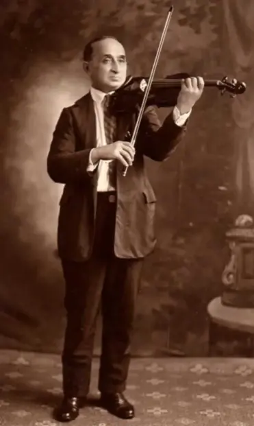 Black and white staged portrait of a man in an ill fitting suit posing with his violin