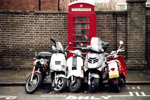 Cinco motocicletas de diversos tipos aparcadas juntas delante de una típica cabina de teléfono roja británica.