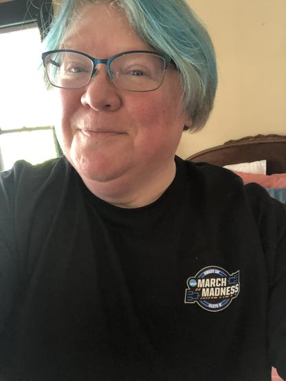 Fat white woman with blue hair and glasses in a black March Madness T-shirt.