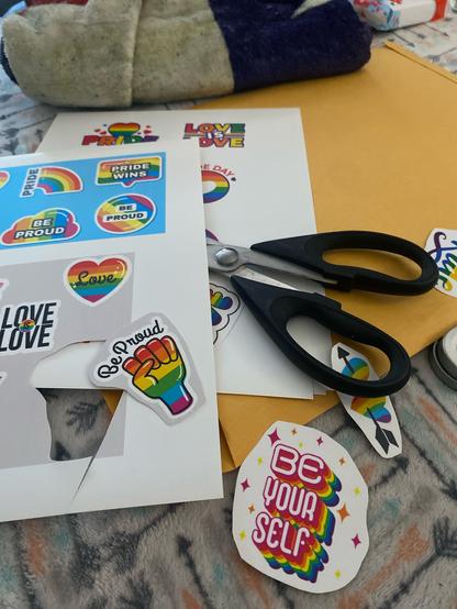 Scissors and paper with pride labels being cut out.