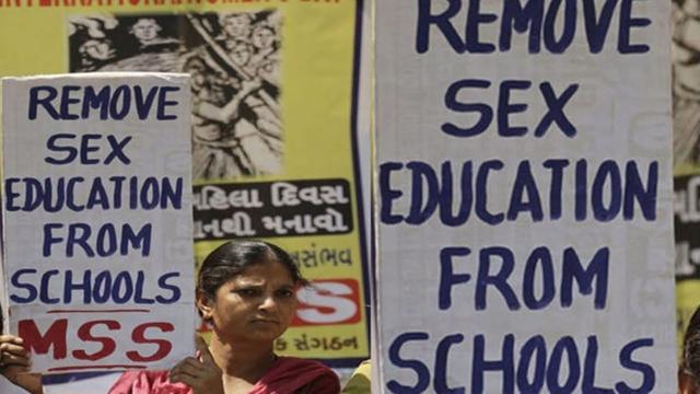 photo of a woman holding a sign reading "remove sex education from schools," standing next to other similar signs