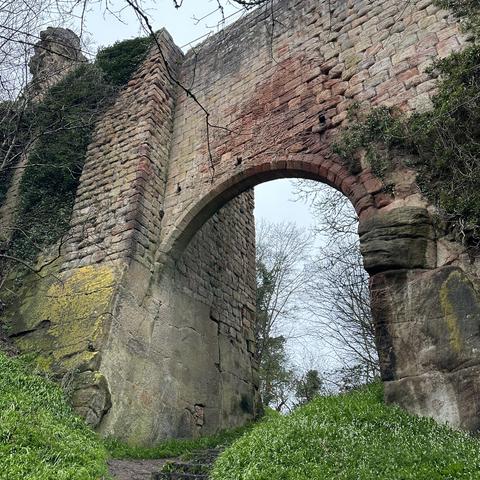 The soaring arched bridge into the partially ruined Roslin Castle in Midlothian, taken from below, looking up. The crumbling sandstone strives to keep gravity at bay, while a tide of wild garlic overwhelms the base of the structure in a swell of green.