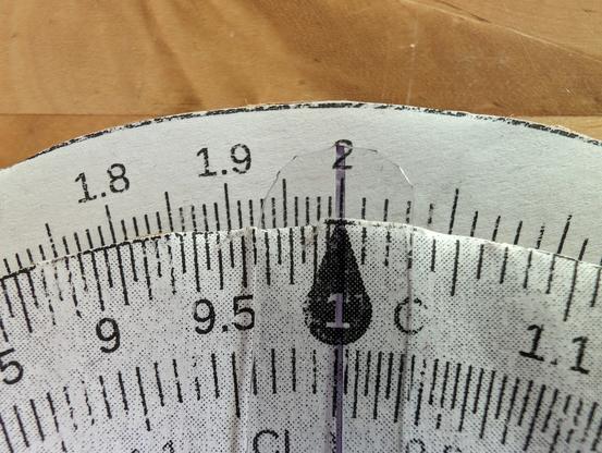 Closeup of a homemade circular slide rule showing 2 on the outer D scale above 1 on the inner C scale.