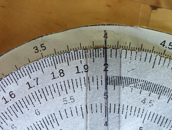Closeup of a homemade circular slide rule showing 4 on the outer D scale above 2 on the inner C scale.