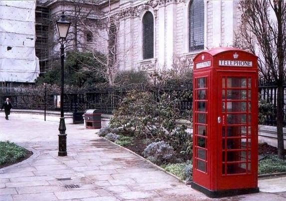 En primer plano, a la derecha, una típica cabina de teléfonos roja británica; al fondo, a la izquierda, un hombre avanza caminando.