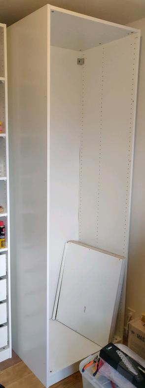 Une photo d'une armoire Ikea PAX décollée du mur; il y a trois tablettes et une tringle posées à l'intérieur