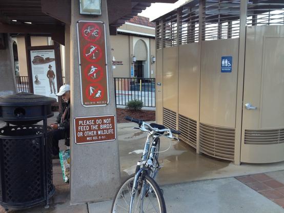 A blue Giant hybrid bicycle, the trusty steed for 20 yrs of Bicycling Monterey’s founder, is parked to the left of a beige “Portland Loo” that was installed on downtown Monterey’s Simoneau Plaza.