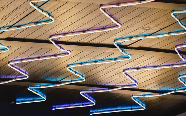 This photo shows several neon light strips, attached to the underside of a wooden walkway down in Mermaid Quay, Cardiff Bay, Wales.

The neon strips are arranged in long, repeating Z patterns.