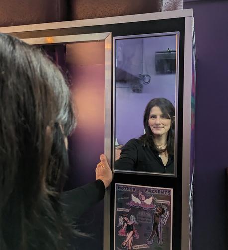 Photographer Chloe Sherman standing outside a photograph looking into a mirror