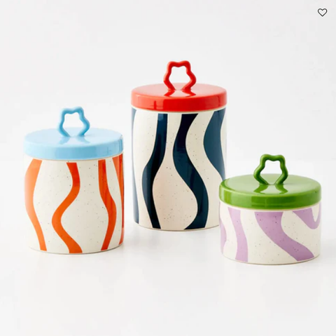 A product photo of three straight sided cylinder shaped canisters with a little wobbly circular handle on the lid. They all have wobbly lines on the jar body and a solid colour for the lid, and all the colours are mismatching. Left is a middle sized canister with orange lines and a sky blue lid; middle is the tallest canister with navy lines and an orange lid; and right is the smallest canister with lilac lines and a green lid.