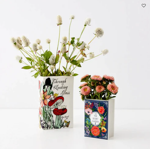 A product photo of two rectangular vases filled with flowers that look like books with hand painted covers. The taller vase has flowers and mushrooms and the text "Through the Looking Glass. The right vase is a little smaller and has flowers surrounding a circle with text "The Secret Garden".
