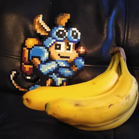 Image of Rocket Knight/Sparkster created with perler beads smiling with his arms crossed standing next to a bunch of bananas. He is small and a pixel sprite and the bananas are real, thus looking huge sitting next to him.