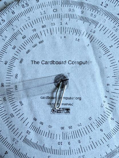 Cardboard and paper circular slide rule, with a paperclip through the centre as an axis.