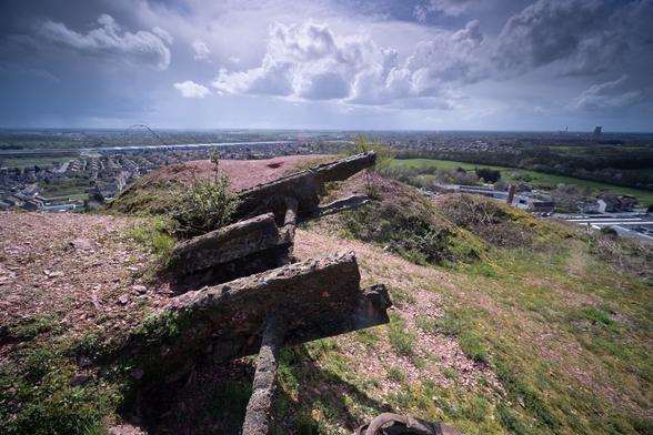 Three rusted metal bars stick out of the top of a hill. From the hill top, the view passes the flat region of Northern France. Extreme wideangle shot taken backlight.