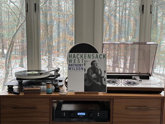 Anthony Wilson - Hackensack West LP cover.

Mostly white. Right half is a black and white photo of Anthony and his guitar.

The black LP plays on a Rega turntable to the left.