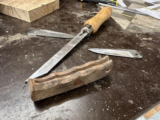 établi, avec des lames aciers de couteau de poche et le manche en cours de montage, avec un ciseau à bois de 3mm fait maison.