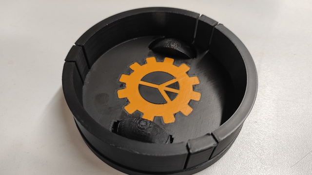 Inside of the mentioned projector lens cap, with the base featuring the printed logo of Hackerspace Pol'and'Rock, which is a vivid orange gear with a peace sign in the center.