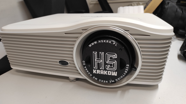 The lens cap placed on the mentioned projector, which is positioned on the table in the softroom.