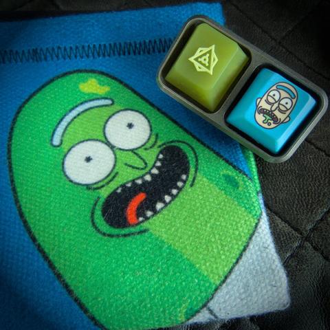 photograph of a fidget toy with a "relish" keycap and a "Rick" from Rick & Morty keycap, next to a hank featuring "Pickle Rick"