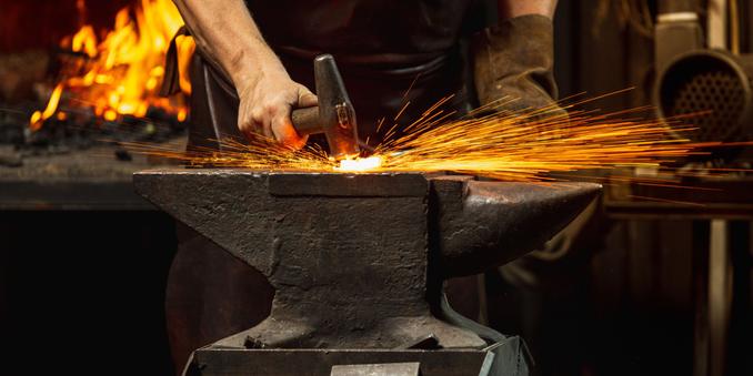 A strong hand striking an anvil with a hammer, creating an explosion of sparks