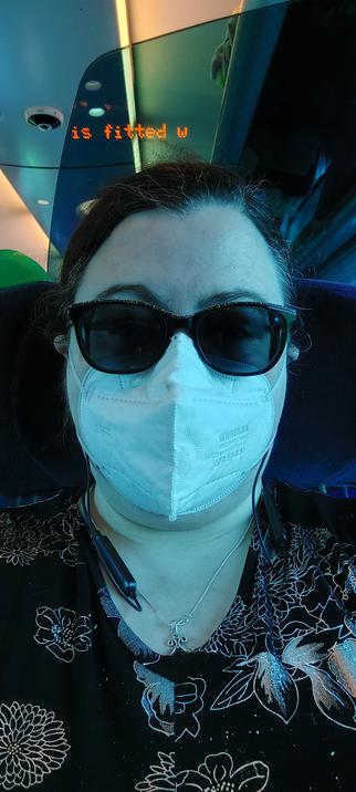 Me a white skinned person wearing sunglasses, a white face mask, hair tied back.