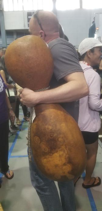 Another view of man carrying a giant Hawaiian ipu gourd through a crowd.