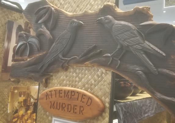 Wood carving of two ʻalalā also known as Hawaiian crows. A wood carved sign beneath them says attempted murder.