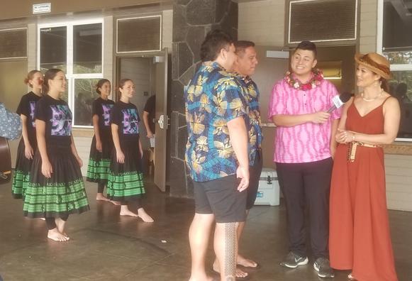 A hula halau (dance troop) of youths stand in ready pose while their kumu (teachers) speak with the local news reporters.