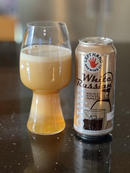 A freshly poured stout glass of creamy beer starts its nitro release process. The dark gold can is to the left with the bright red left hand logo of its namesake