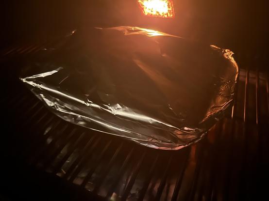 A foil-wrapped item on a grill with soft illumination from flames in the background.
