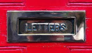 A silver letterbox sits in the centre of a cropped picture of a red door. The word "LETTERS" is on the letterbox. A slight pattern is visible, but key details of the door's pattern are not shown. A reflection is shown of the body of the photographer. The letters of the wording have blue surrounding them, showing it's aged.